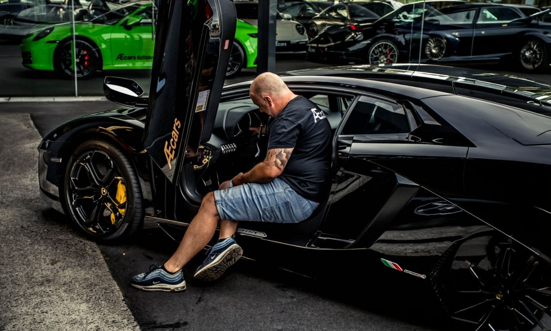Medewerker van AEcars begeleidt een klant bij een exclusieve sportwagen