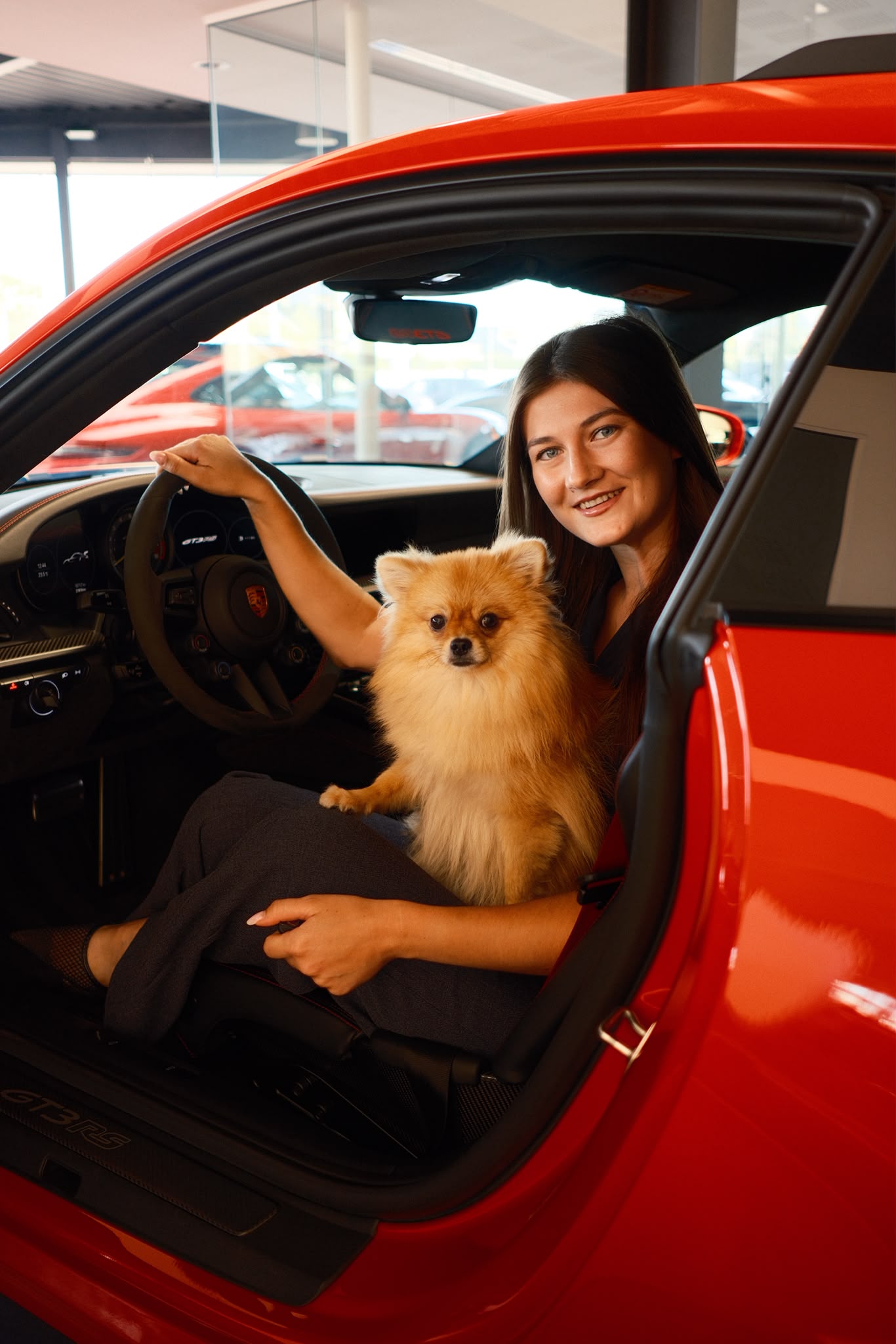 Julie van het salesteam van AEcars met een hondje in een rode sportwagen