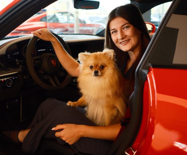 Julie van het salesteam van AEcars met een hondje in een rode sportwagen